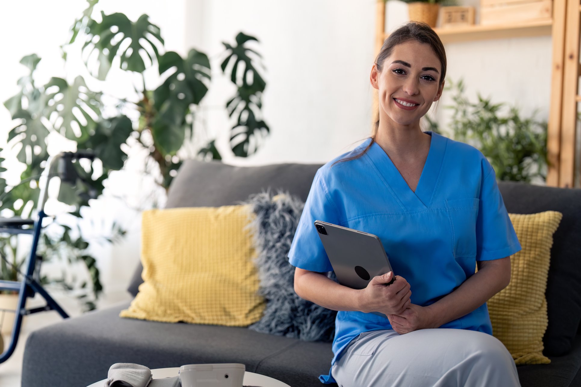DRK-Pflegerin sitzt mit einem Arbeits-Tablet auf einer Couch