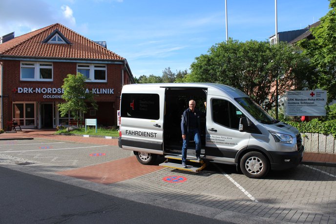 Am Auto der Fahrzeugflotte von der DRK Nordsee-Reha-Klinik steht ein Mann an der offenen Fahrzeugtür
