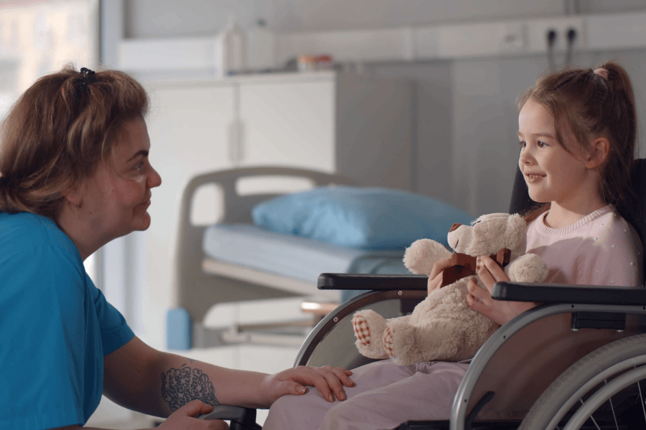 Pflegerin und kleines Mädchen im Rollstuhl unterhalten sich in der Klinik