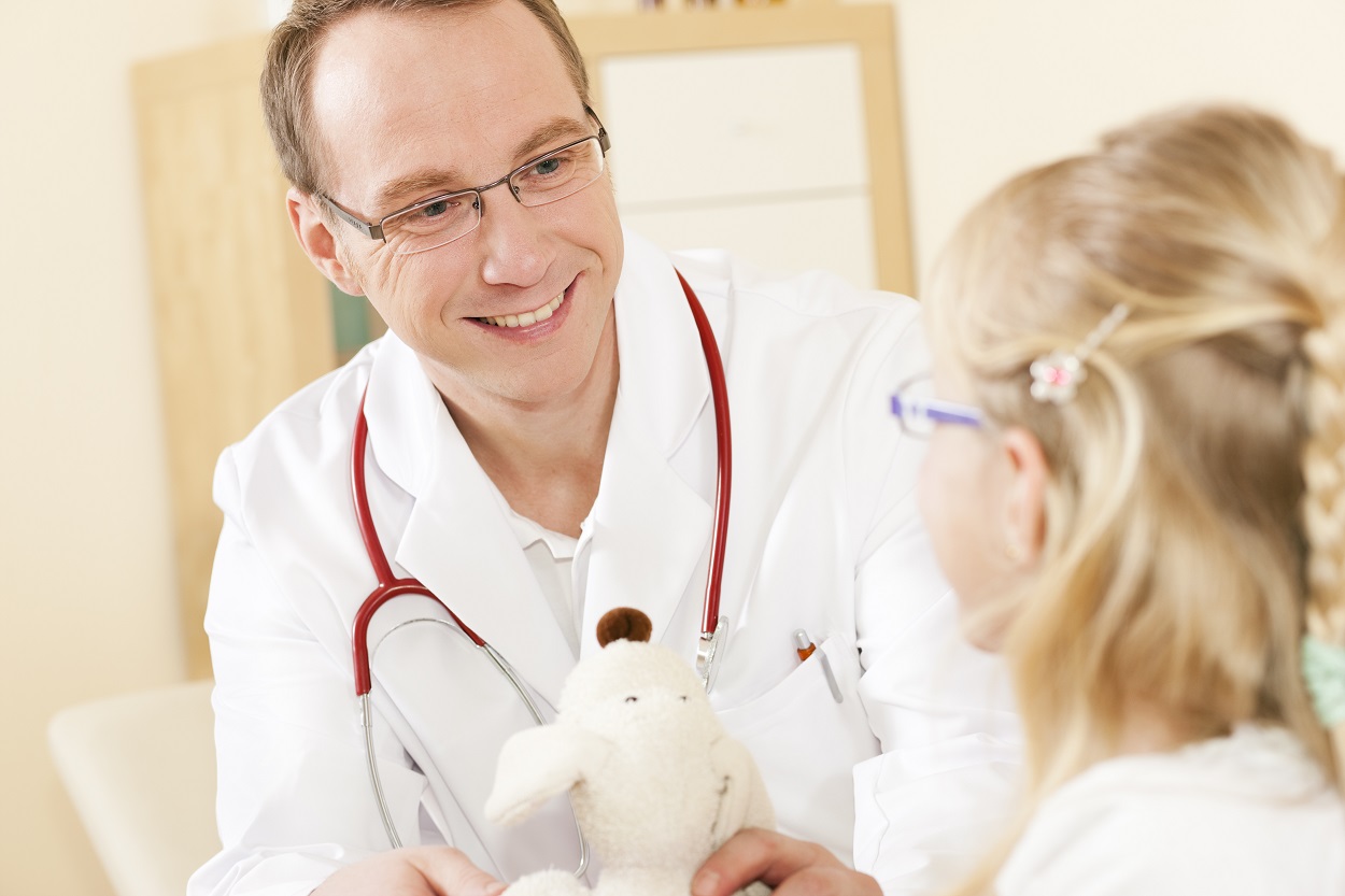 DRK-Arzt sitzt bei einer jungen Patientin und hält einen Teddybär in der Hand